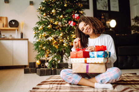 A young woman on the background of a Christmas tree with gifts, with a tablet has a video call or video chat.の写真素材
