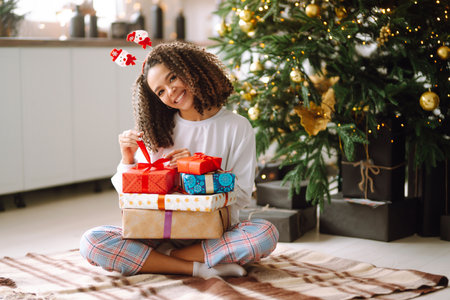 A young woman on the background of a Christmas tree with gifts, with a tablet has a video call or video chat.の写真素材