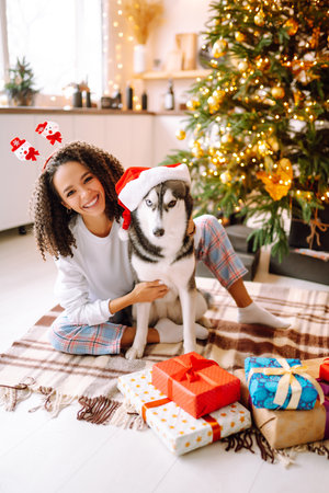 Beautiful woman playing and having fun with her dog while sitting near the christmas tree.の写真素材