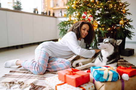 Beautiful woman playing and having fun with her dog while sitting near the christmas tree.の写真素材