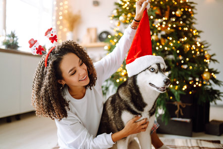Beautiful woman playing and having fun with her dog while sitting near the christmas tree.の写真素材