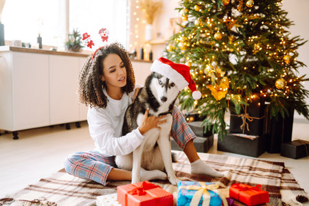 Beautiful woman playing and having fun with her dog while sitting near the christmas tree.の写真素材