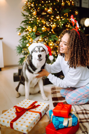 Beautiful woman playing and having fun with her dog while sitting near the christmas tree.の写真素材
