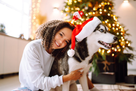 Beautiful woman playing and having fun with her dog while sitting near the christmas tree.の写真素材