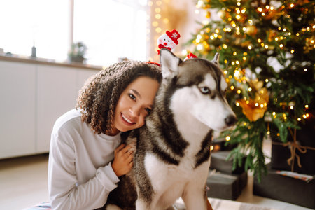Beautiful woman playing and having fun with her dog while sitting near the christmas tree.の写真素材