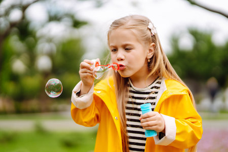 Cute little girl in the autumn on a walk blowing soap bubbles. Childhood, active rest, lifestyle concept.の写真素材