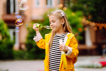 Cute little girl in the autumn on a walk blowing soap bubbles. Childhood, active rest, lifestyle concept.の写真素材