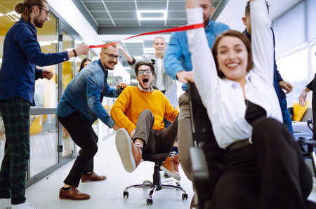 Young colleagues group having fun together, riding on chairs in officeの写真素材
