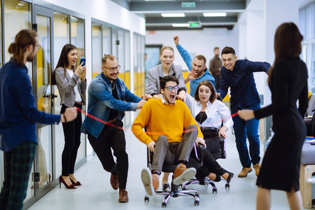 Young colleagues group having fun together, riding on chairs in officeの写真素材