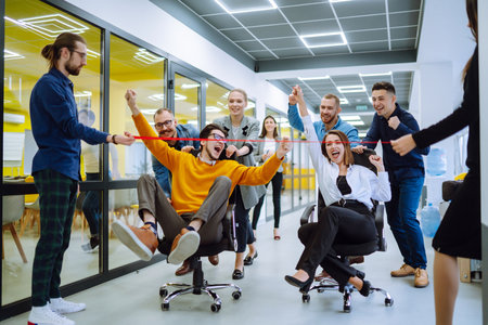 Young colleagues group having fun together, riding on chairs in officeの写真素材