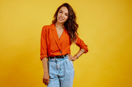Portrait of young girl posing on yellow background. Pretty woman wears a carrot blouse and jeans.の写真素材