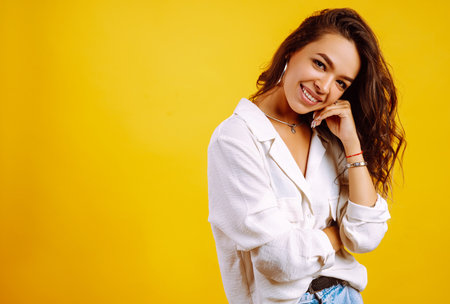 Portrait of young girl posing on yellow background. Pretty woman wears a carrot blouse and jeans.の写真素材