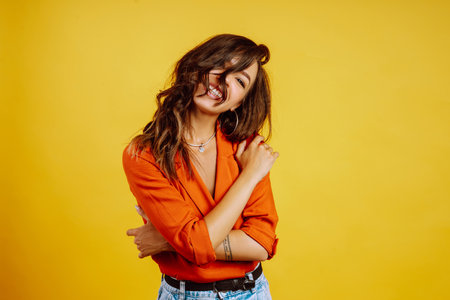 Portrait of young girl posing on yellow background. Pretty woman wears a carrot blouse and jeans.の写真素材