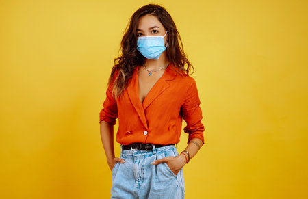 Portrait of young girl posing on yellow background. Pretty woman wears a carrot blouse and jeans.の写真素材