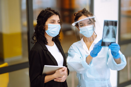 Two business colleagues in protective face mask discussing work related matters on an office.の写真素材