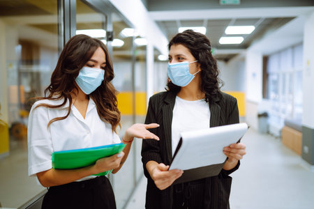 Two business colleagues in protective face mask discussing work related matters on an office.の写真素材