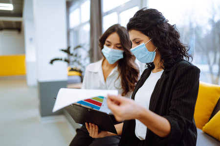 Two business colleagues in protective face mask discussing work related matters on an office.の写真素材