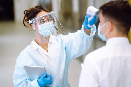 temperature screening office workers. Disease control expert in visor with an Infrared thermometer.の写真素材