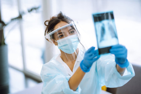 A female doctor in visor and protective gloves examines an X-ray of a patientの写真素材