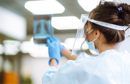 A female doctor in visor and protective gloves examines an X-ray of a patient