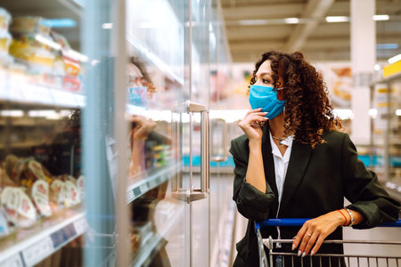 Young woman wearing face mask buying in supermarket. Shopping during the pandemic. Covid-2019.の写真素材