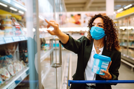 Young woman wearing face mask buying in supermarket. Shopping during the pandemic. Covid-2019.の写真素材