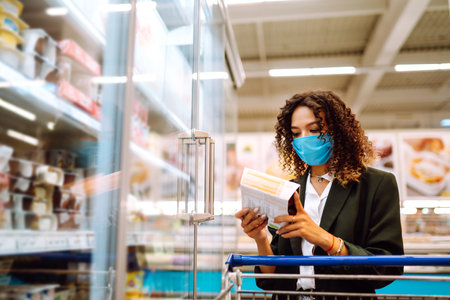 Young woman wearing face mask buying in supermarket. Shopping during the pandemic. Covid-2019.の写真素材