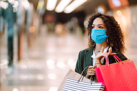 Young woman wearing protection face mask against coronavirus after shopping in the mall. Covid-2019.の写真素材