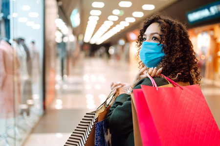 Young woman wearing protection face mask against coronavirus after shopping in the mall. Covid-2019.の写真素材