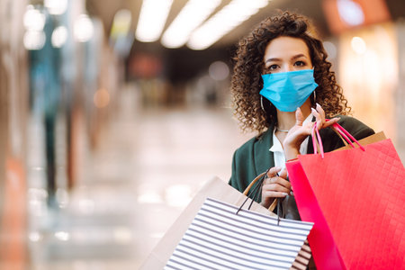 Young woman wearing protection face mask against coronavirus after shopping in the mall. Covid-2019.の写真素材