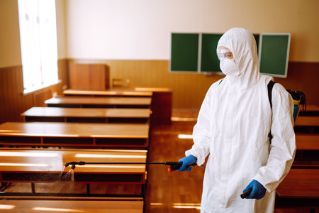 Man in protective hazmat suit washes school desk during coronavirus pandemic. COVID-19.の写真素材