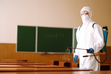 Man in protective hazmat suit washes school desk during coronavirus pandemic. COVID-19.の写真素材