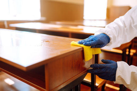 Portrait of man in protective hazmat suit with spray chemicals disinfecting school class. COVID-19.の写真素材