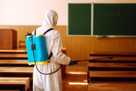 Man in protective hazmat suit washes school desk during coronavirus pandemic. COVID-19.の写真素材