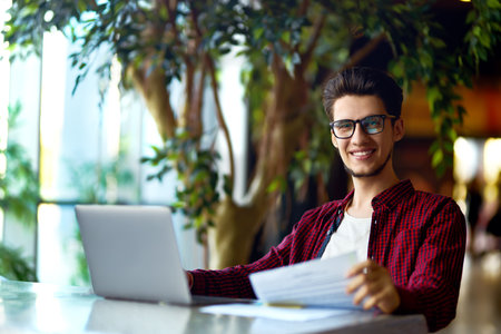 Smiling young hipster man in glasses with laptop on the table. Programmer, web developer.の写真素材