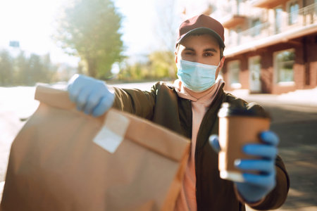 Courier in medical mask and gloves delivers on a scooter a bag of food in quarantine city....