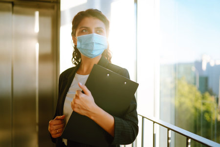 Portrait of businesswoman in protective face mask during virus epidemic while standing near elevator