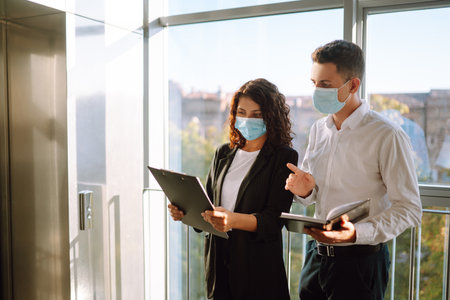 Two coworkers in protective face masks discussing project. Work in office during quarantine. covidの写真素材