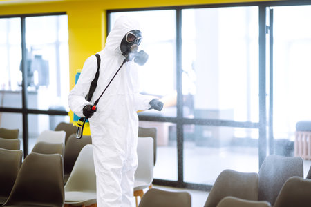 Cleaning and disinfection of office to prevent COVID-19, Man in protective hazmat suit washes officeの写真素材