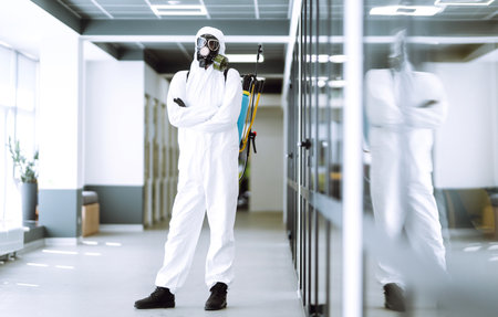 Man in protective hazmat suit and mask works on a computer in an empty office. Covid-19.の写真素材