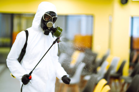 Cleaning and disinfection of office to prevent COVID-19, Man in protective hazmat suit washes officeの写真素材