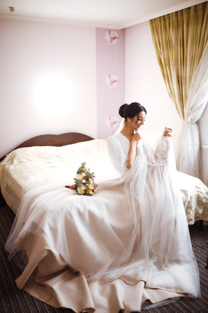 Stylish happy bride is getting ready in the morning. Happy newlywed woman in bedroom. fashion bride.の写真素材