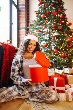 Smiling African American woman using laptop, sitting near Christmas tree with card, shopping onlineの写真素材