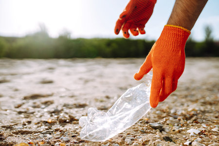 Trash on the beach. Men hand wearing protective gloves collects bottle plastic on sea beach.の写真素材
