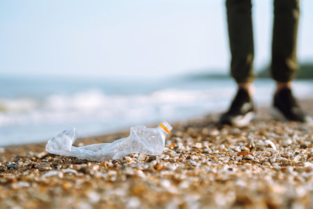 Trash on the beach. Men hand wearing protective gloves collects bottle plastic on sea beach.の写真素材