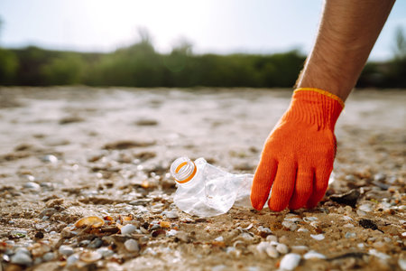 Trash on the beach. Men hand wearing protective gloves collects bottle plastic on sea beach.の写真素材
