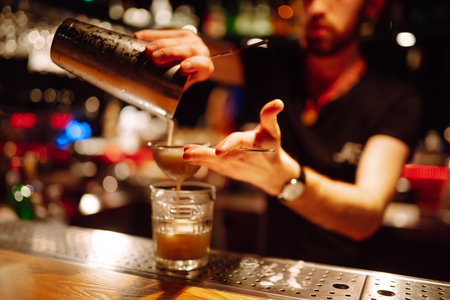 Expert barman is making refreshing cocktail at night club. Bartender pouring strong and fresh drink.