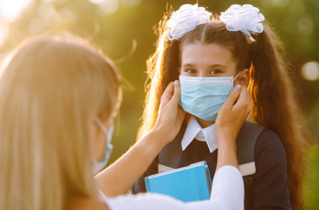 Little girl and mom in medical mask during covid-19 at sunset. Virus, pandemic, outbreak and epidemic.の写真素材
