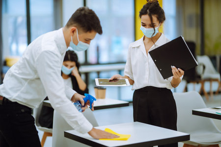 Cleaning and disinfection of the desktop. Man in protective sterile mask cleans the work desk.の写真素材