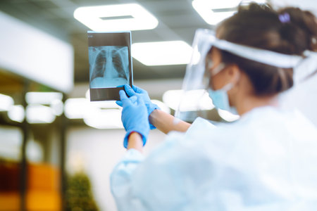 A female doctor in visor and protective gloves examines an X-ray of a patient